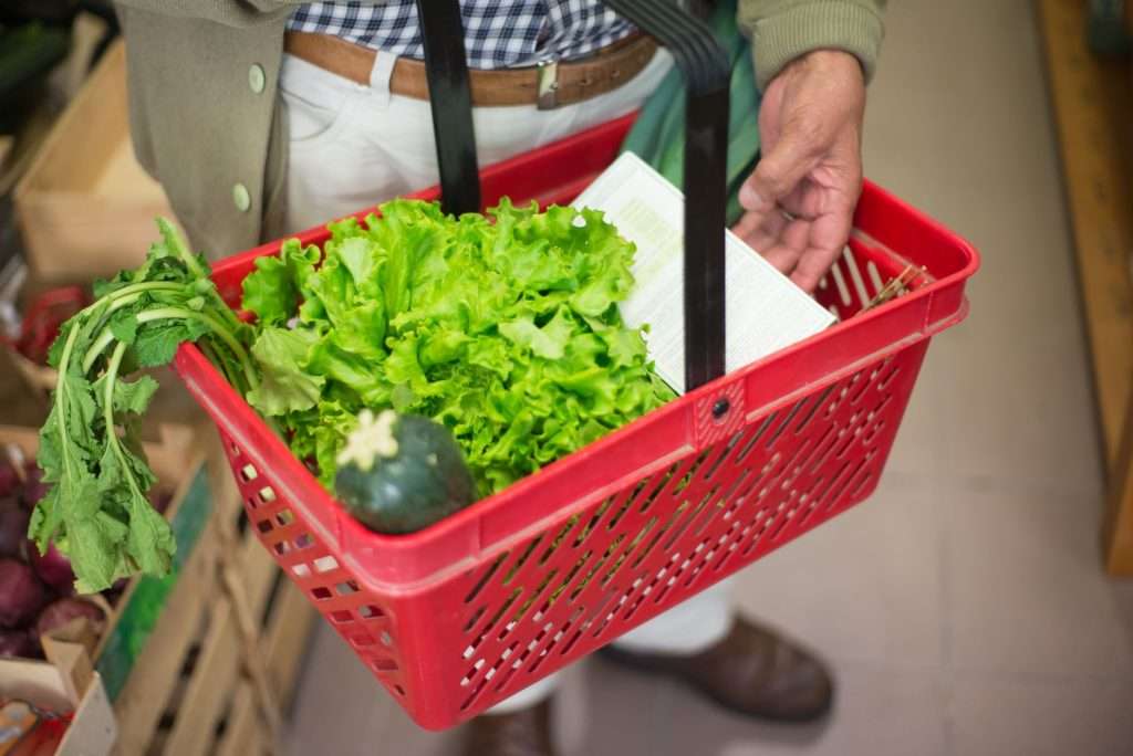 Ultra Bann Close-up of a hand carrying a shopping basket filled with fresh greens in a market