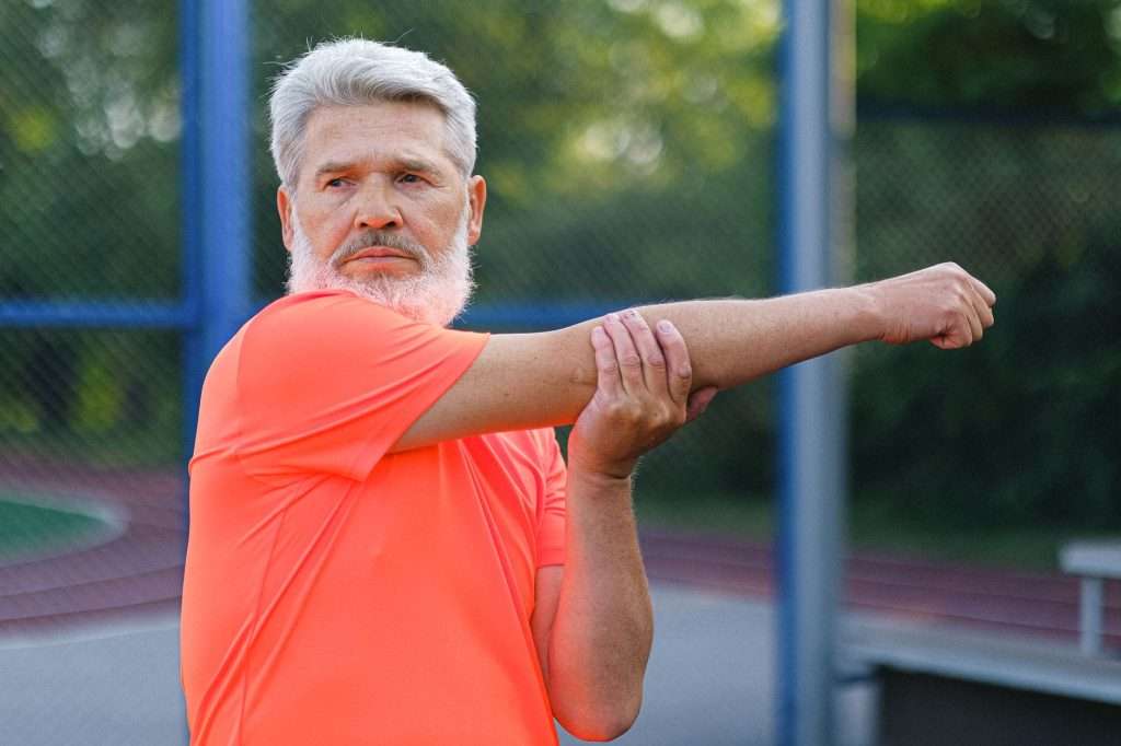 Ultra Bann Stylish mature male athlete with modern hairstyle and beard in sportswear stretching before training on stadium